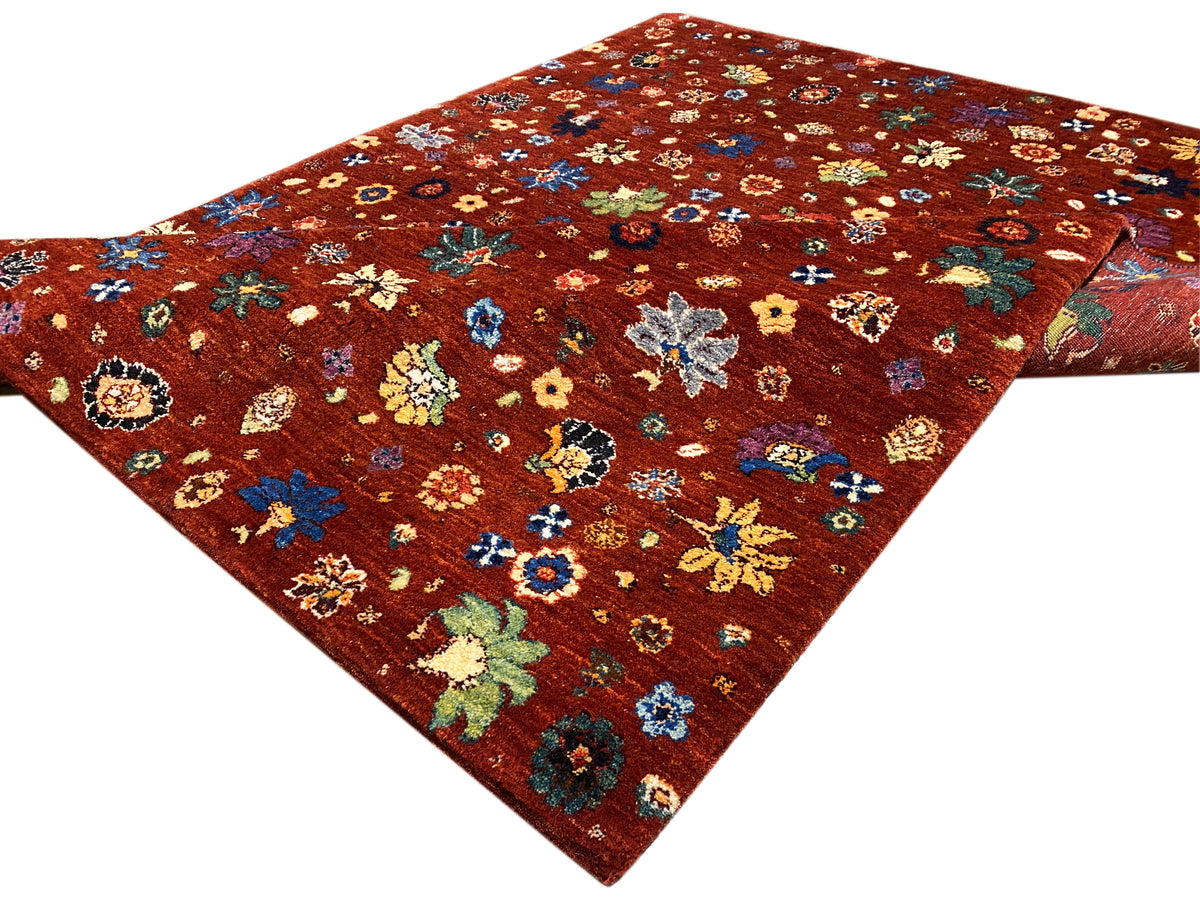 Teppich mit rötlich-braunem Grund und buntem Blumenmuster, dreiviertel-gesehene Kante.