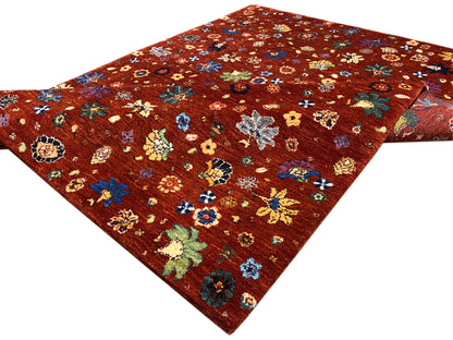 Teppich mit rötlich-braunem Grund und buntem Blumenmuster, dreiviertel-gesehene Kante.