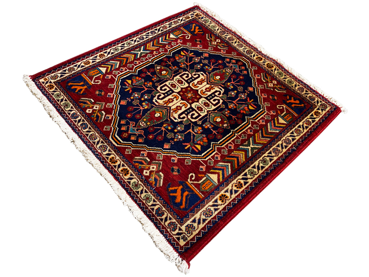 斜めから見た63x60cmのラグ：濃紺の中央、赤い縁、フリンジ